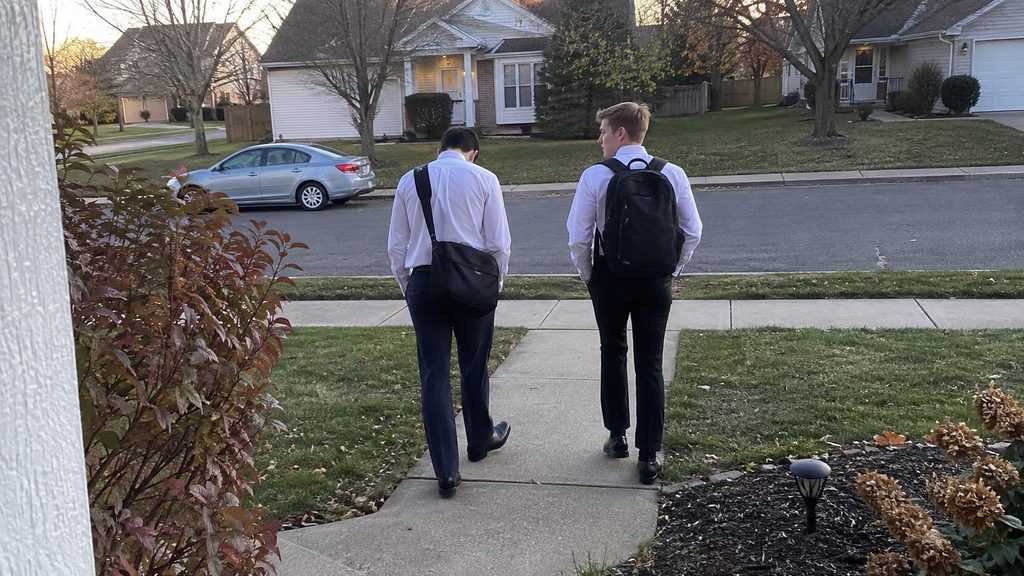 Two Latter-day Saint missionaries walking after a lesson with one visibly moved and the other quietly thoughtful